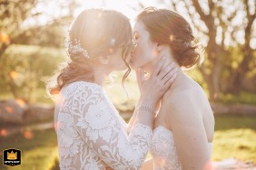   At Newton Hall in Northumberland, UK, the couple share a tender kiss at sunset, glowing against the vibrant evening sky.